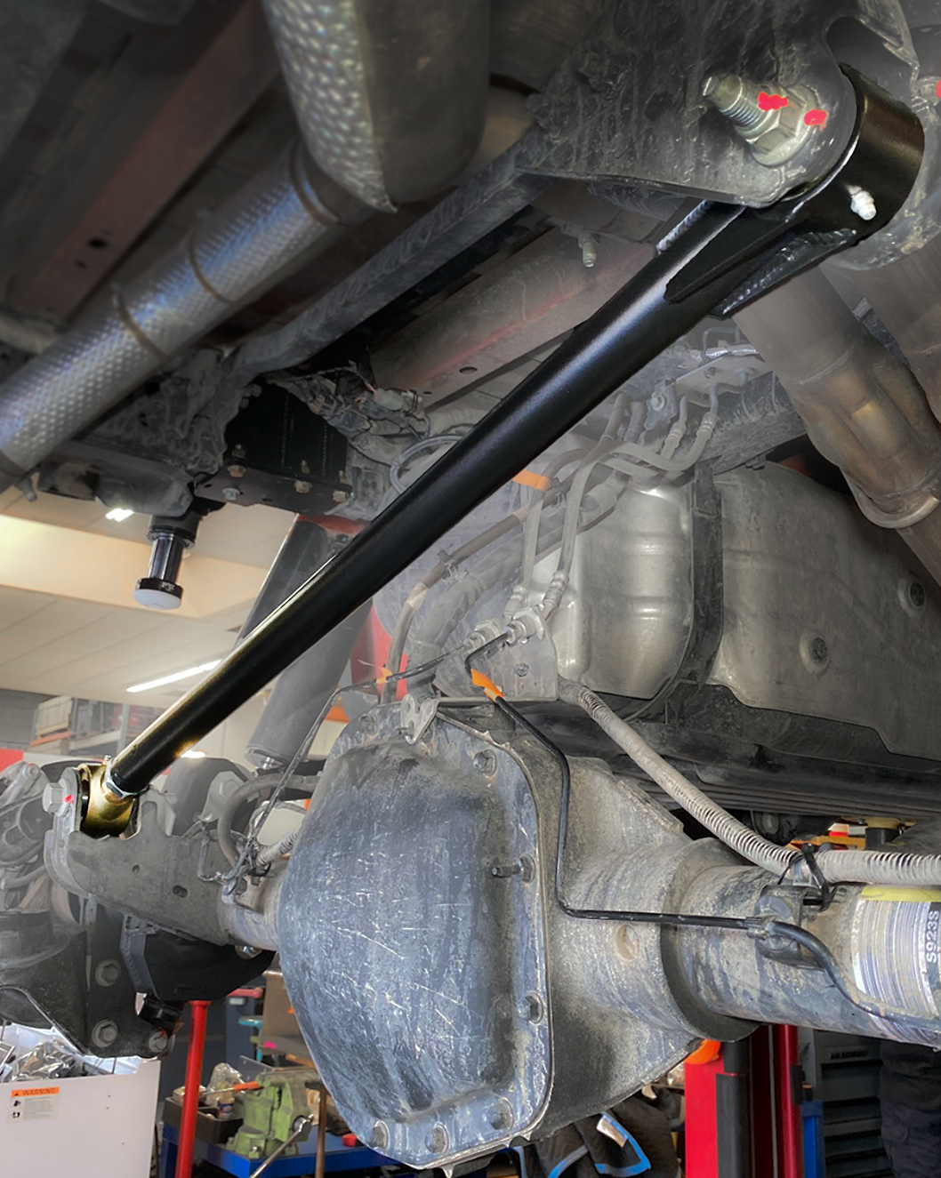 Adjustable Johnny Joint panhard bar installed under a 2021-2026 Ford Raptor, running across the rear axle beside the exhaust