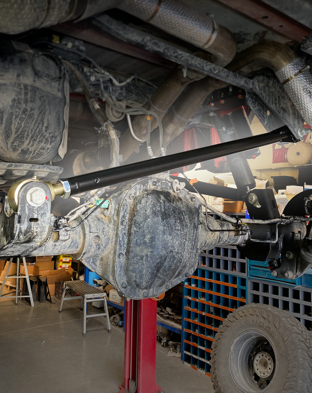Wide view from under a Gen 3 Raptor on the lift showing the full span of the installed black panhard bar