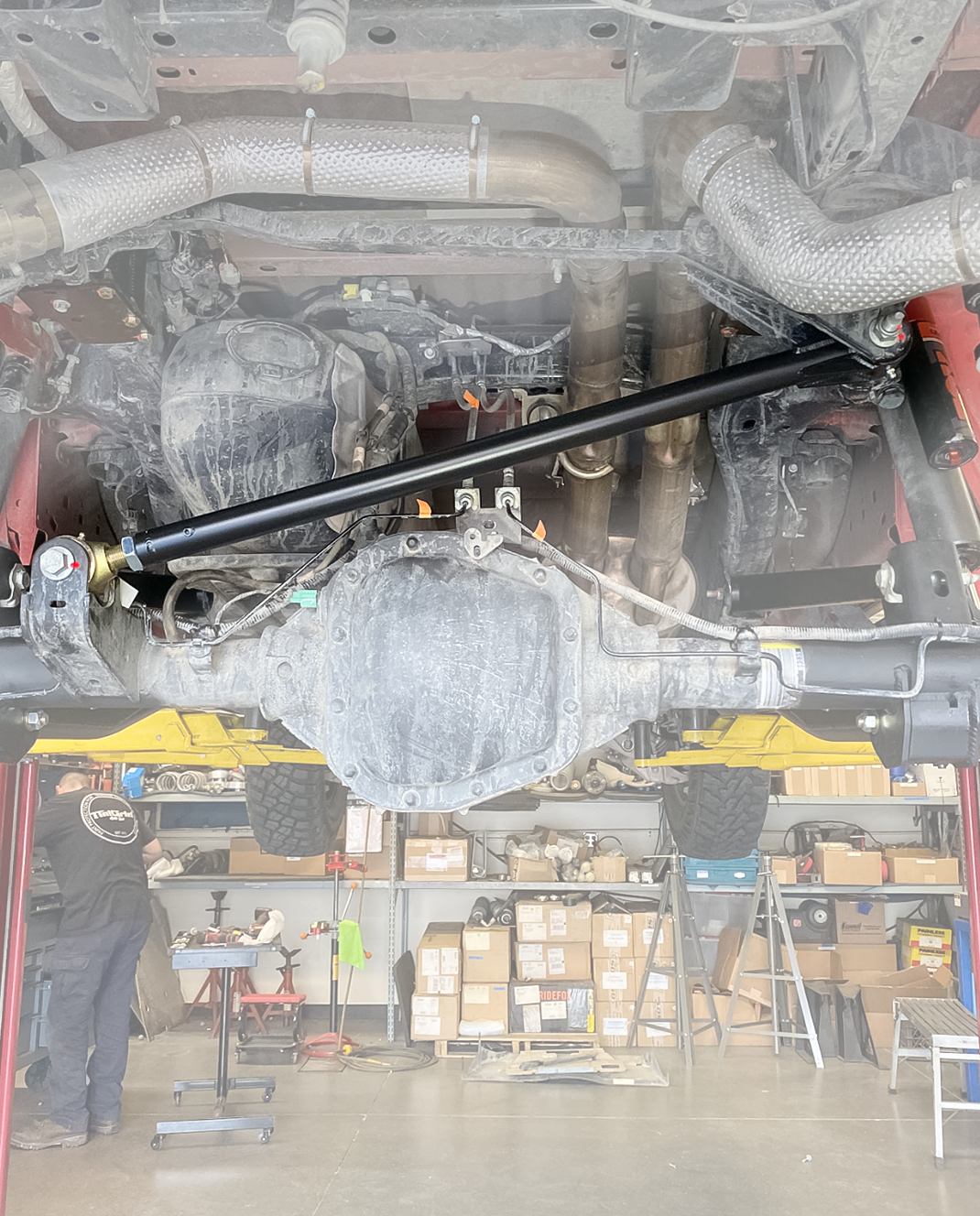 Gen 3 Raptor rear axle viewed from below with the adjustable track bar fitted, shop floor visible behind