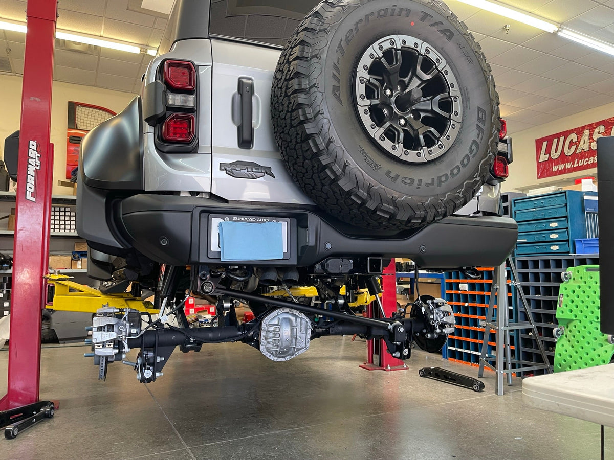 Rear three-quarter view of a Ford Bronco Raptor on the lift with the rear suspension exposed