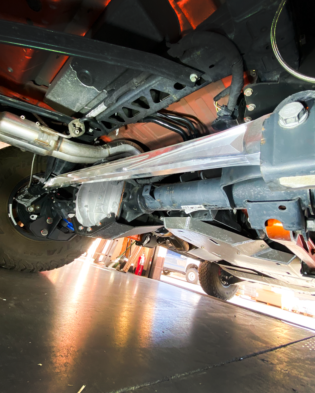 Raw billet panhard bar under a Bronco Raptor with the exhaust above, viewed from below