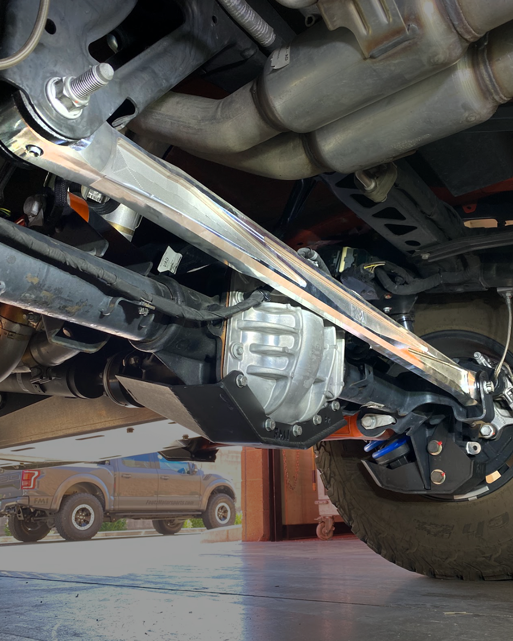 Low-angle shot of a raw billet aluminum panhard bar running across a Bronco Raptor rear axle