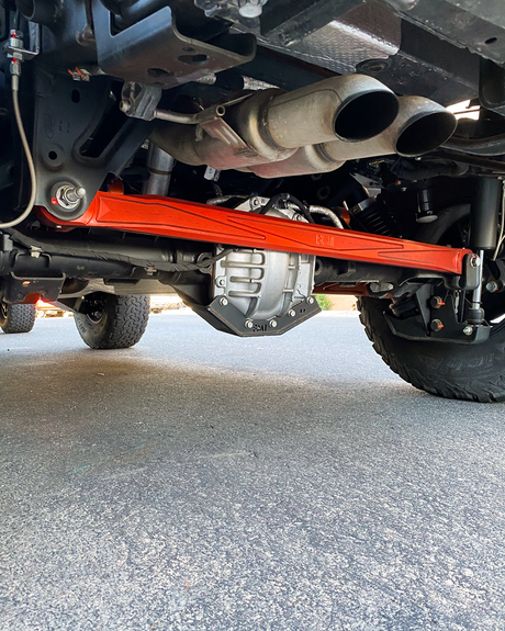 Orange anodized FMI billet panhard bar installed across the rear axle of a Ford Bronco Raptor, seen from behind the truck