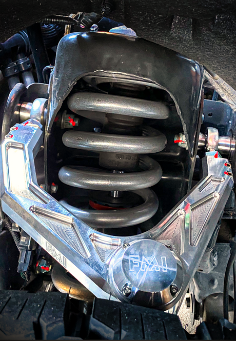 Raw billet aluminum FMI upper control arm with bearing cap spanning the coil spring on a Gen 3 Ford Raptor