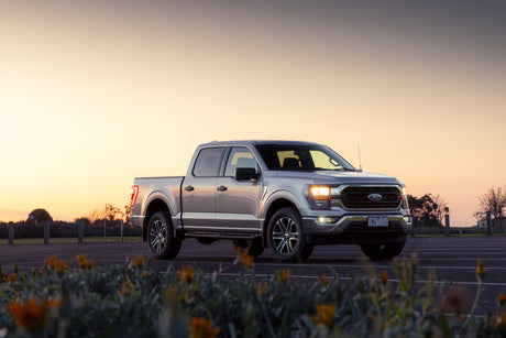 Silver 2021-2023 Ford F-150 crew cab parked at sunset with headlights on