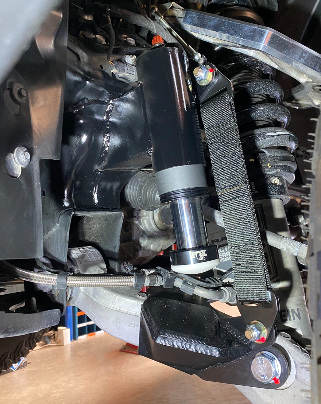 drivers side of Stock lower arm Front Limit Strap with Bump Stop Stock installed on a ram TRX 