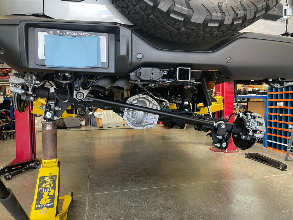 Rear of a Ford Bronco Raptor on the shop lift with the rear axle supported on jacks for the arm install