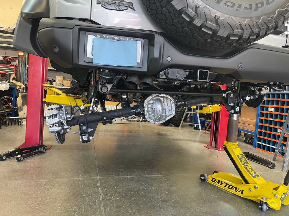 Bronco Raptor rear axle lowered on jacks under the truck, rear arm install in progress, second angle