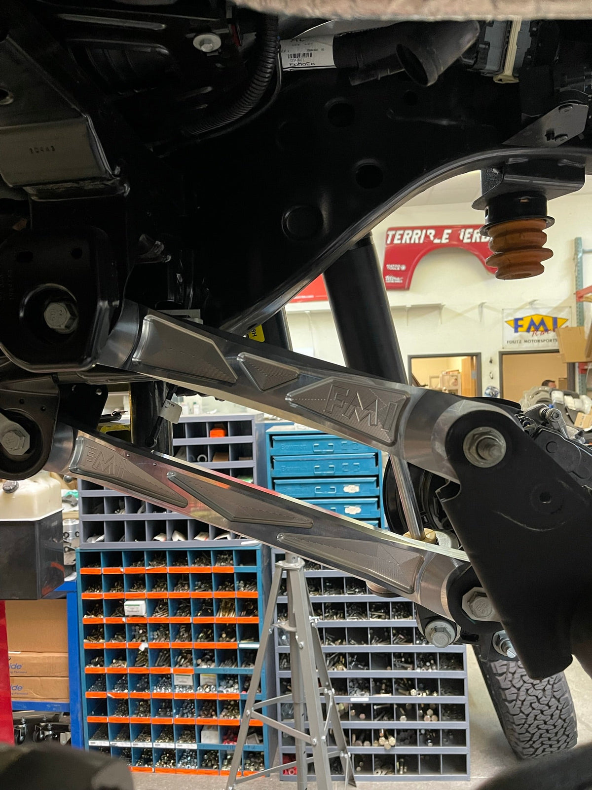 Raw billet aluminum upper and lower rear arms installed on a Ford Bronco Raptor, seen from below on the lift
