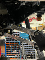 Raw billet aluminum upper and lower rear arms installed on a Ford Bronco Raptor, seen from below on the lift