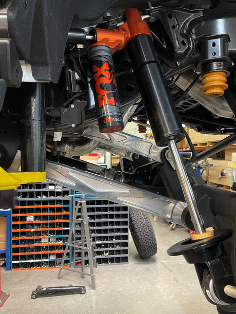 Raw billet rear lower arm under the factory FOX shock and coil spring on a Bronco Raptor