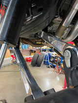 Raw billet rear arms seen from behind the rear wheel of a Bronco Raptor in the shop