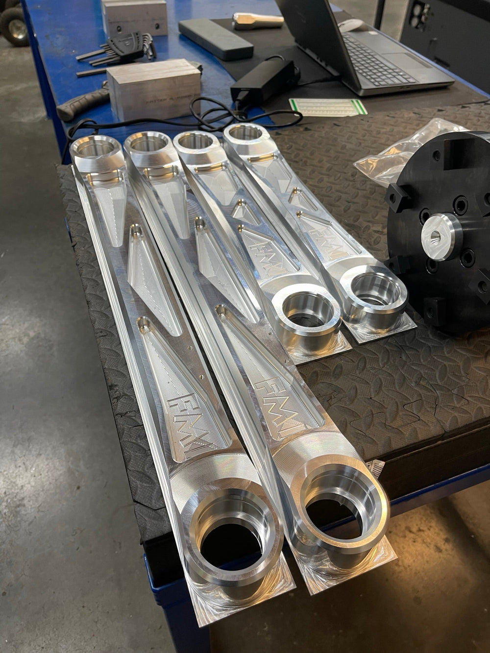 Four raw billet Bronco Raptor rear arms, two upper and two lower, laid out on a workbench
