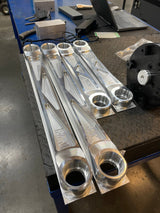 Four raw billet Bronco Raptor rear arms, two upper and two lower, laid out on a workbench