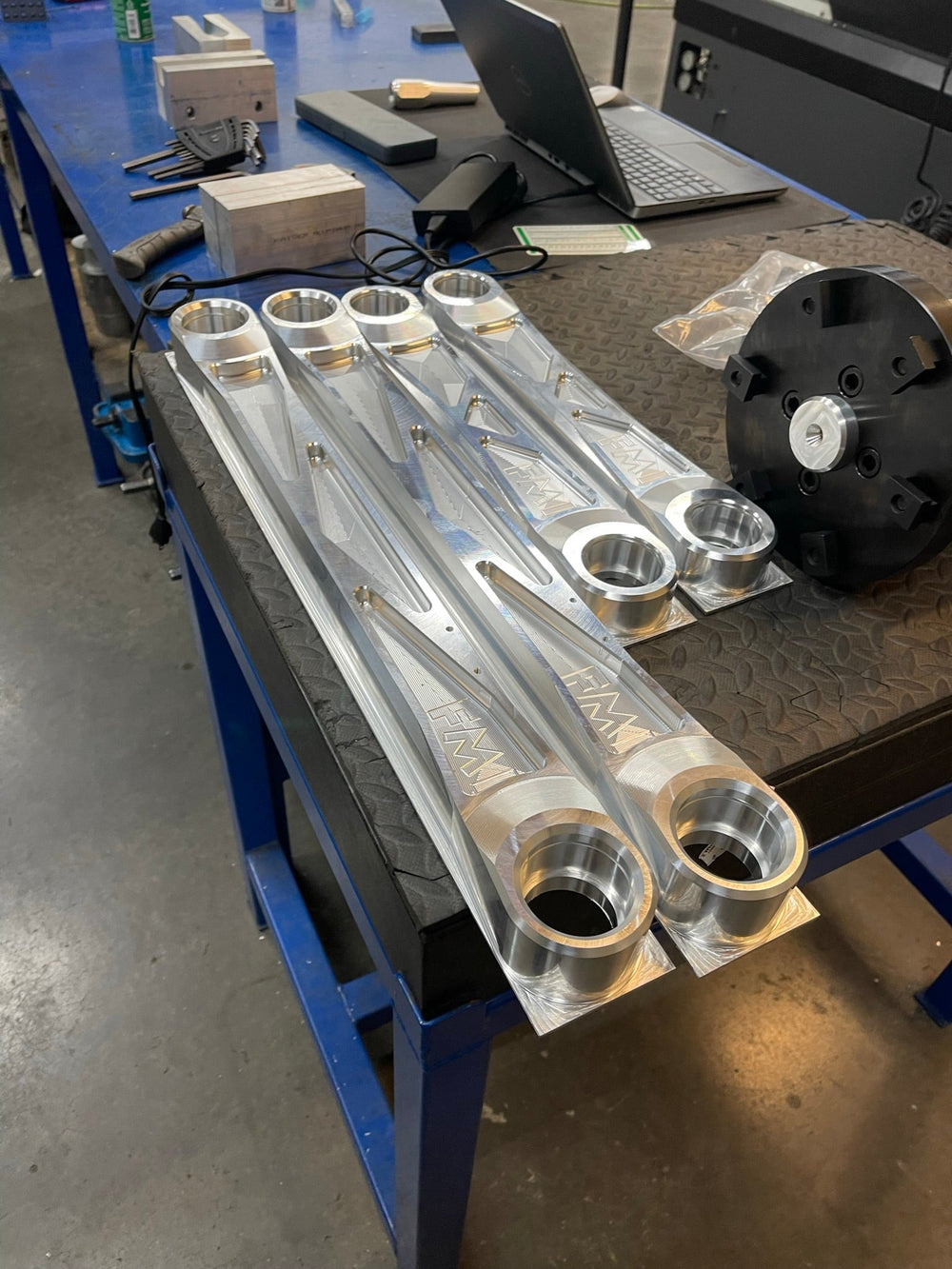 Raw billet rear arm set on the workbench showing the uniball bores, angled view