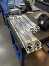 Raw billet rear arm set on the workbench showing the uniball bores, angled view