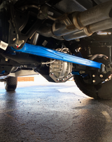 Blue anodized billet panhard bar installed under a Ford Bronco Raptor, outdoor low view