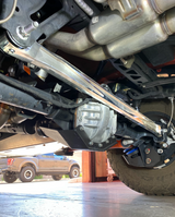 Raw billet aluminum panhard bar installed across the Bronco Raptor rear axle, seen from below in the shop