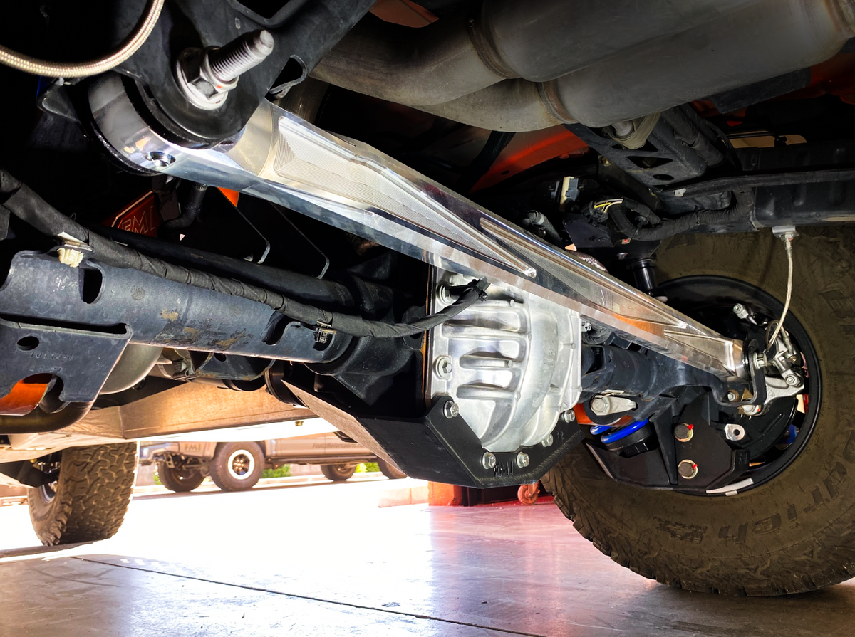 Raw billet Bronco Raptor panhard bar spanning the rear axle, seen from the rear wheel side