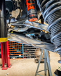 Raw billet aluminum rear links installed on a Ford Bronco Raptor on the shop lift, next to the factory FOX rear shock