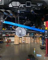 Blue anodized billet panhard bar across the full width of a Bronco Raptor rear axle on the lift