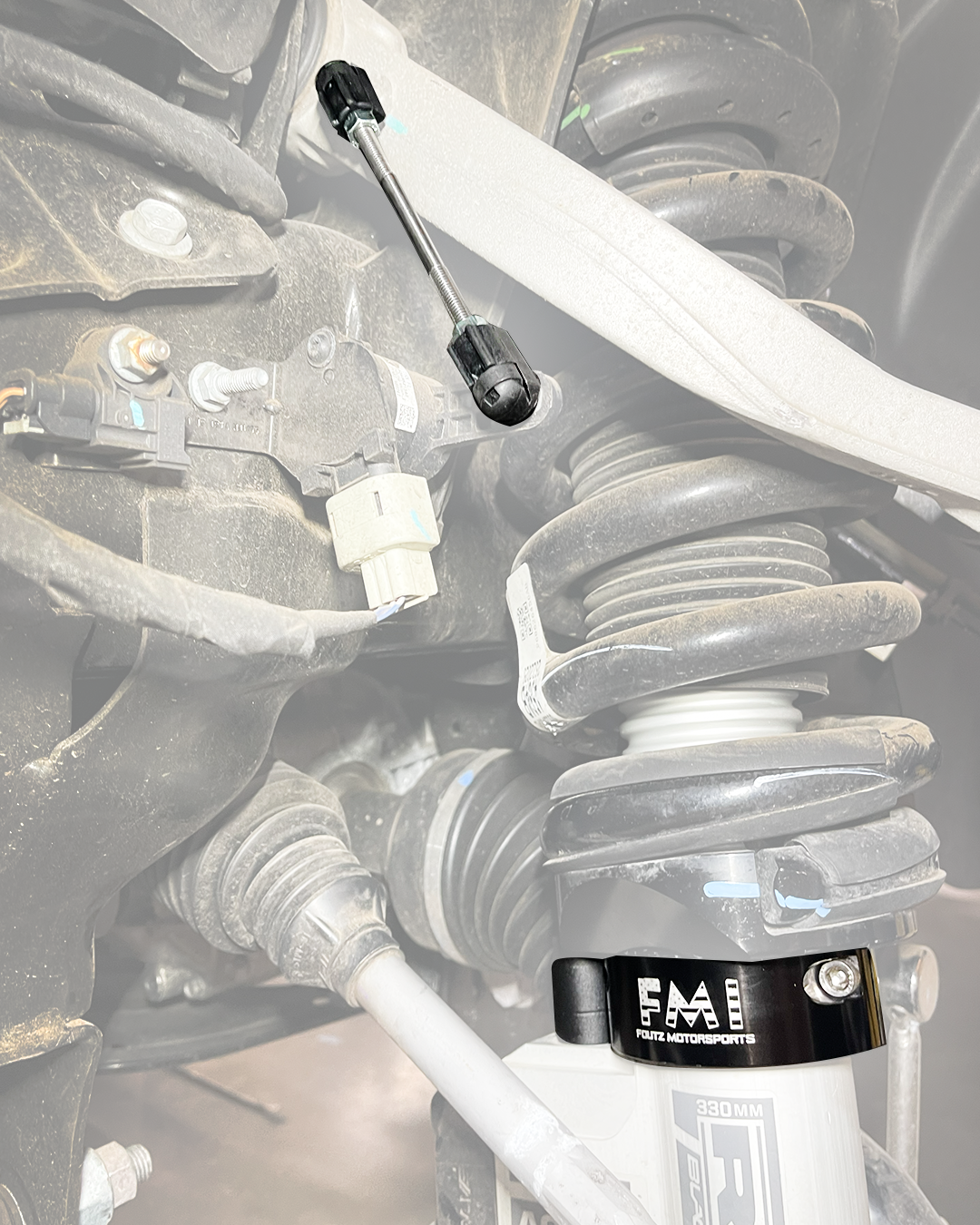 Wheel well view of the 2027 Ram TRX front suspension with the ride height sensor connector rod highlighted and the 2.5" collar below the coil spring